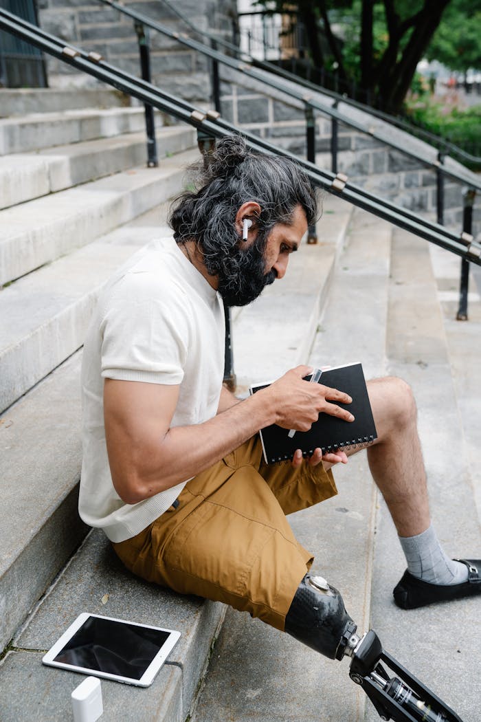 Seated man with prosthetic leg reading on steps, displaying focused contemplation.